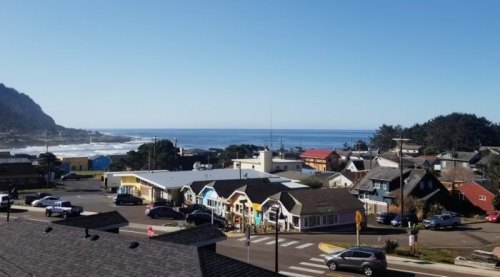 A coastal town with colorful buildings, a clear blue sky, and waves crashing on the shore in the background.