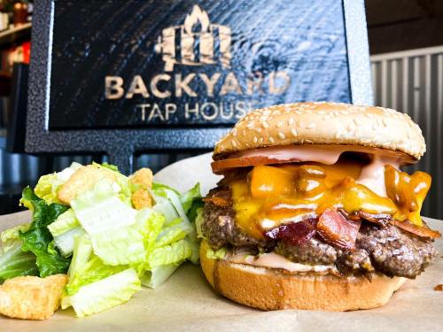 A juicy burger with cheese, bacon, and toppings, served with a side of fresh lettuce and croutons at Backyard Tap House.