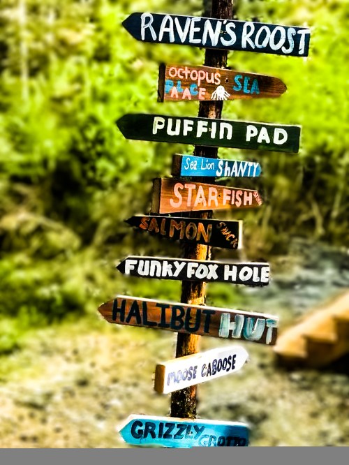 Colorful wooden signs pointing to various whimsical locations in a natural setting.