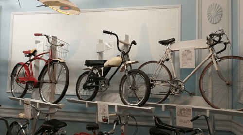 Four vintage bicycles displayed on shelves against a light blue wall, showcasing different styles and designs.