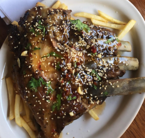 A plate of grilled ribs topped with sauce, sesame seeds, and herbs, served with French fries.