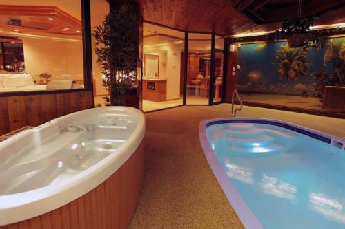 A luxurious indoor spa area featuring a hot tub and a swimming pool, surrounded by tropical decor and warm lighting.