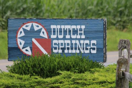 Sign for Dutch Springs, featuring a blue background with a red and white design, surrounded by greenery and fields.