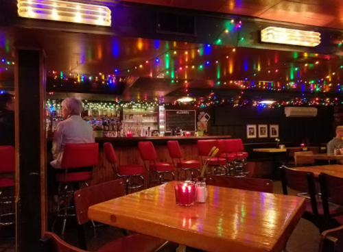 Cozy bar interior with colorful string lights, red stools, and wooden tables, creating a warm, inviting atmosphere.