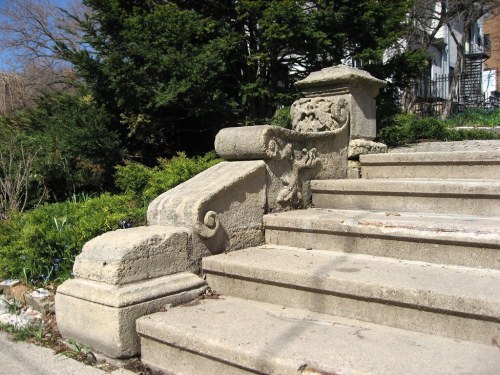 Stone steps with ornate railings, surrounded by greenery and trees, showcasing intricate architectural details.