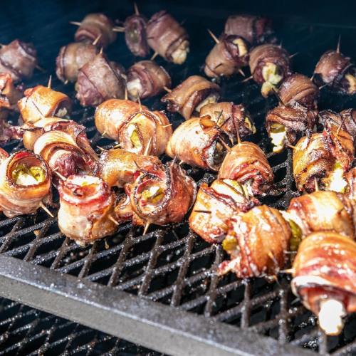 Bacon-wrapped jalapeño poppers grilling on a barbecue, sizzling and smoky.