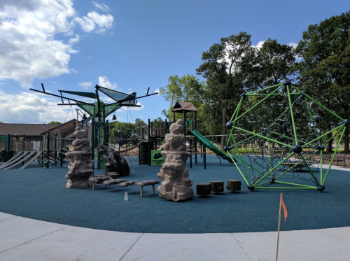 A colorful playground featuring climbing structures, rock formations, and slides on a sunny day.