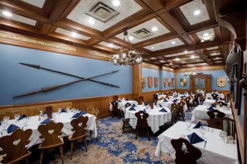 Elegant dining room with wooden decor, white tablecloths, blue walls, and decorative shields.