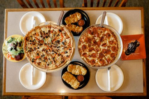 A table with two pizzas, a salad, and breadsticks, all served on plates.