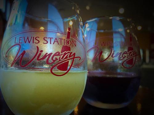 Two wine glasses with the logo "Lewis Station Winery," one filled with white wine and the other with red wine.