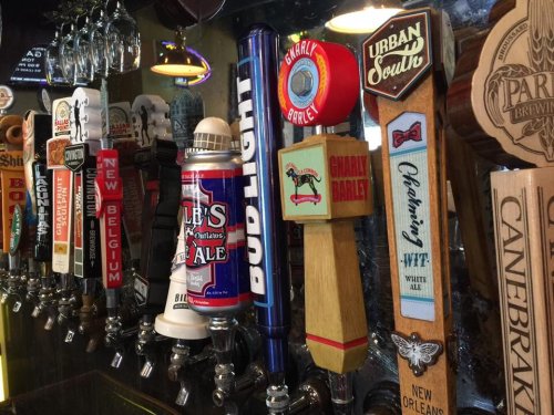 A variety of beer taps featuring different brands and styles lined up on a bar counter.