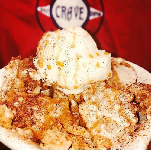 A bowl of dessert featuring cinnamon, crumbled cake, and a scoop of vanilla ice cream on top.