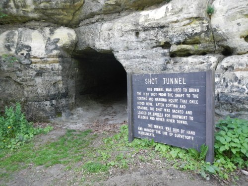 Entrance to a stone tunnel with a wooden sign explaining its historical use for transporting lead shot.