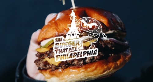 A hand holding a juicy burger with cheese and toppings, featuring a playful graphic overlay.