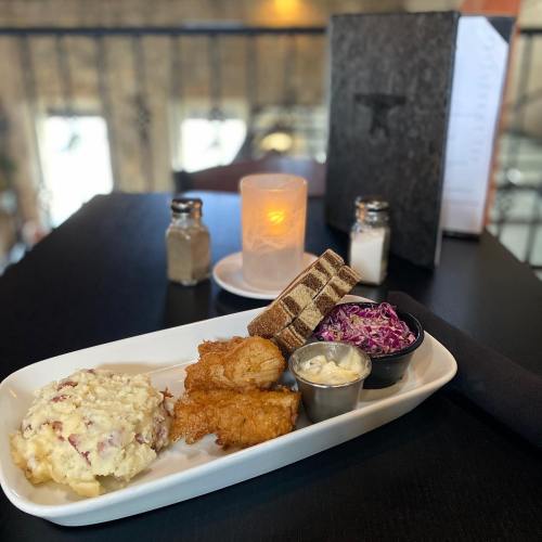 A plate with fried fish, mashed potatoes, coleslaw, and bread, set on a table with a candle and menu in the background.