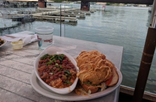 A plate of food featuring beans and a sandwich, with a scenic view of a lake and docks in the background.