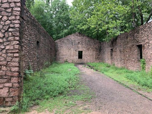 Ruins of a stone building surrounded by greenery, with a pathway leading through the center.
