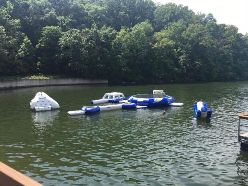 Inflatable water toys float on a calm lake surrounded by lush green trees.