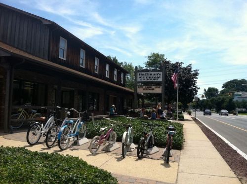 A quaint library with a wooden exterior, bicycles parked out front, and people enjoying the outdoors nearby.