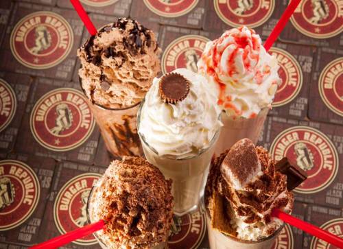 Five delicious milkshakes topped with whipped cream and straws, arranged on a branded table surface.