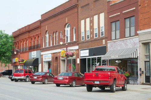 A row of brick storefronts with parked red trucks in front, showcasing a small-town shopping district.