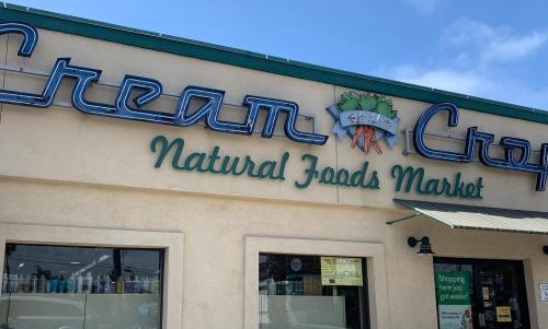 Sign for "Cream Crop Natural Foods Market" on a building exterior, featuring blue neon letters and green accents.