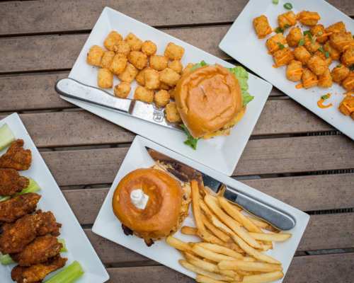 A spread of delicious food including burgers, fries, tater tots, and chicken wings on white plates.