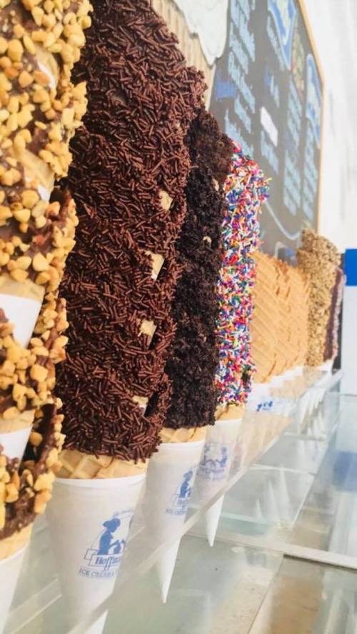 A row of ice cream cones topped with various toppings like sprinkles, nuts, and chocolate, displayed in a shop.