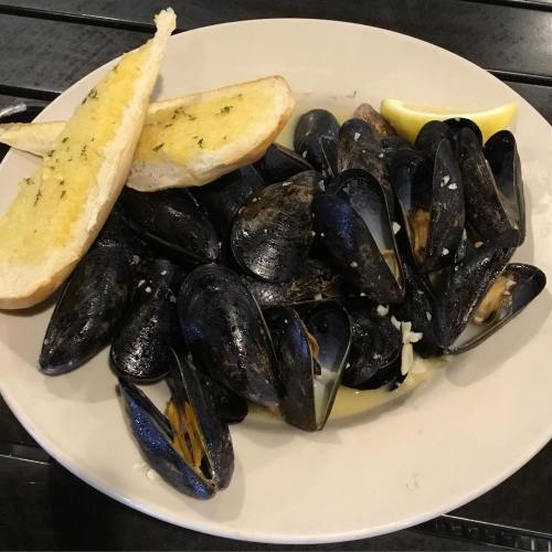 A plate of mussels in broth, served with two slices of garlic bread and a lemon wedge.