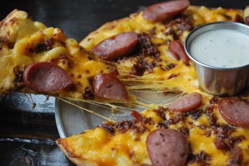 A close-up of a cheesy pizza topped with sausage slices, served with a side of dipping sauce.