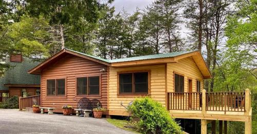 A wooden cabin with a green roof, surrounded by trees, featuring a porch and flower pots.