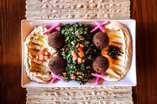 A platter featuring hummus, tabbouleh, and falafel balls, garnished with pink pickled onions and drizzled with olive oil.