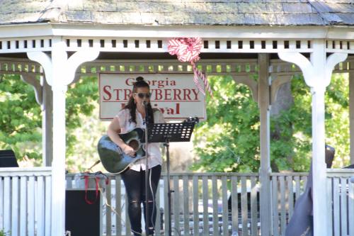 A musician performs on stage at the Georgia Strawberry Festival, playing guitar in a gazebo.