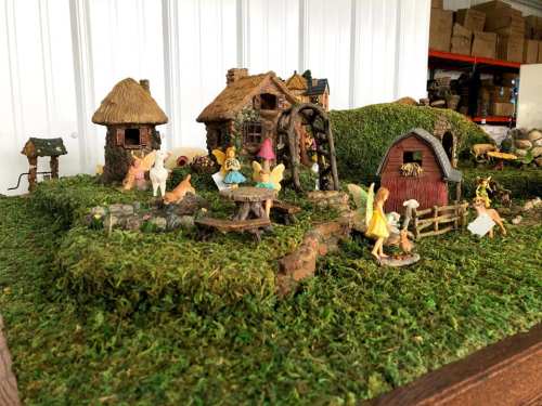 A whimsical fairy village with tiny houses, fairies, and lush greenery, set on a moss-covered landscape.