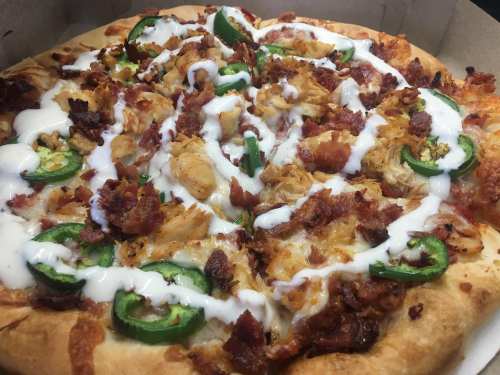 Close-up of a pizza topped with chicken, bacon, jalapeños, and drizzled with ranch dressing.