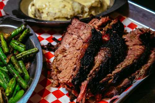 A plate of sliced smoked brisket with green beans and mashed potatoes on a checkered tray.