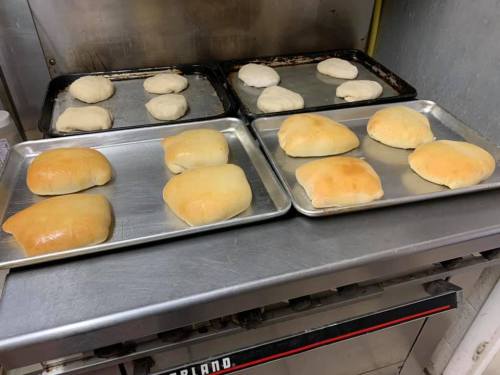 Trays of freshly baked bread rolls cooling on metal sheets in a kitchen.