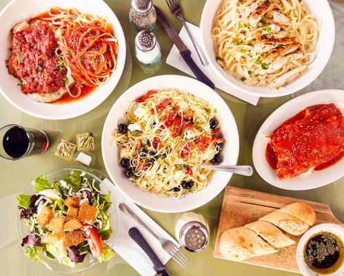 A table spread with various pasta dishes, salad, garlic bread, and condiments, showcasing a delicious Italian meal.