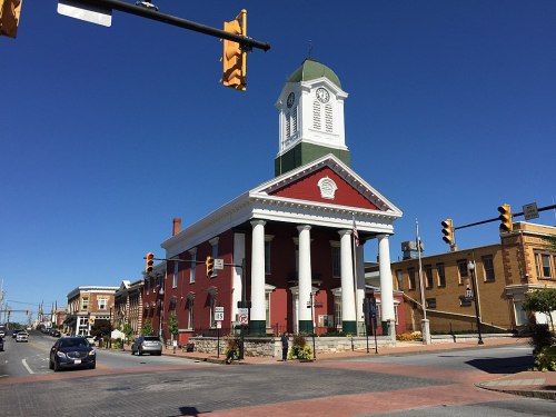 Historic red building with white columns and clock tower, set against a clear blue sky, near traffic lights and street.