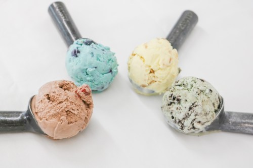 Four ice cream scoops in metal scoops: chocolate, mint chocolate chip, vanilla, and blue raspberry.
