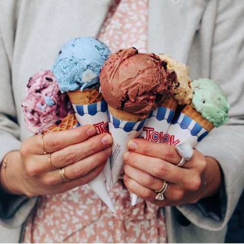 A person holds five ice cream cones with various colorful flavors, including blue, brown, green, and pink.