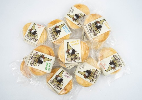 A collection of individually wrapped savory pies with various labels, including chicken and mushroom, bacon, and egg.