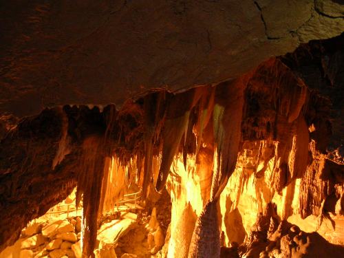 Stalactites and stalagmites in a dimly lit cave, with warm orange lighting illuminating the rocky formations.
