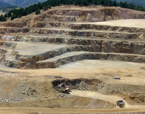 A large open-pit mine with terraced layers, heavy machinery, and a rugged landscape in the background.