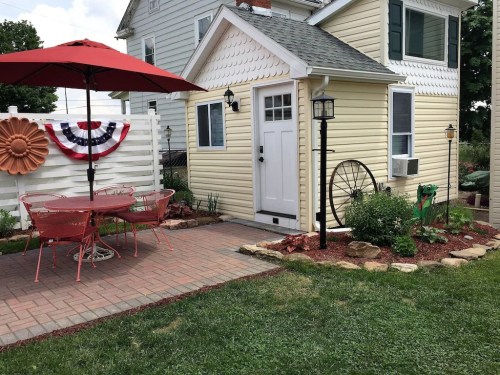 A charming yellow house with a patio, red umbrella, and decorative elements, surrounded by a well-kept garden.