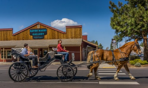 A horse-drawn carriage passes by the Raven Makes Gallery in Sisters, Oregon, with passengers enjoying the ride.