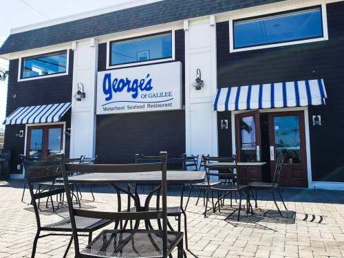 Exterior of George's of Galilee, a waterfront seafood restaurant, featuring outdoor seating and striped awnings.