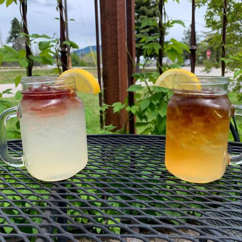 Two mason jar drinks on a black metal table: one clear with lemon and a red layer, the other iced tea with lemon.