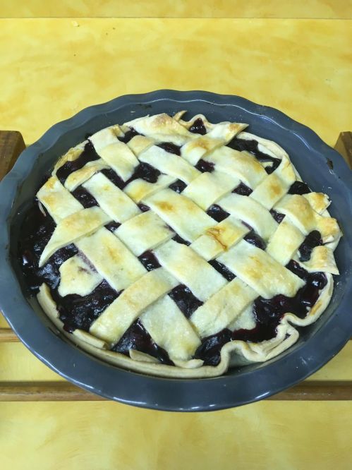 A freshly baked berry pie with a golden lattice crust, sitting in a gray pie dish on a yellow countertop.