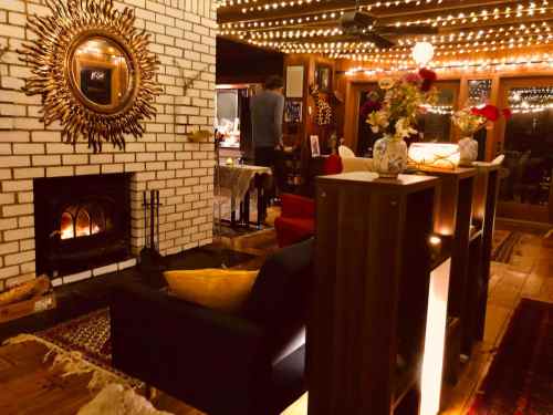 Cozy living room with a fireplace, decorative mirror, and warm lighting, featuring a person in the background.